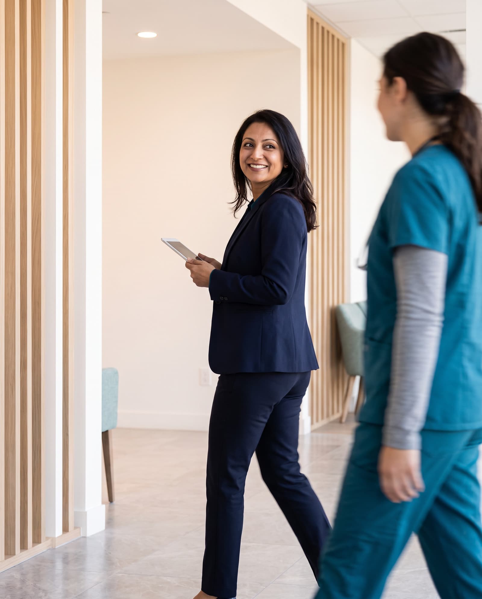 A practice manager walking through a clinic hallway with a tablet
