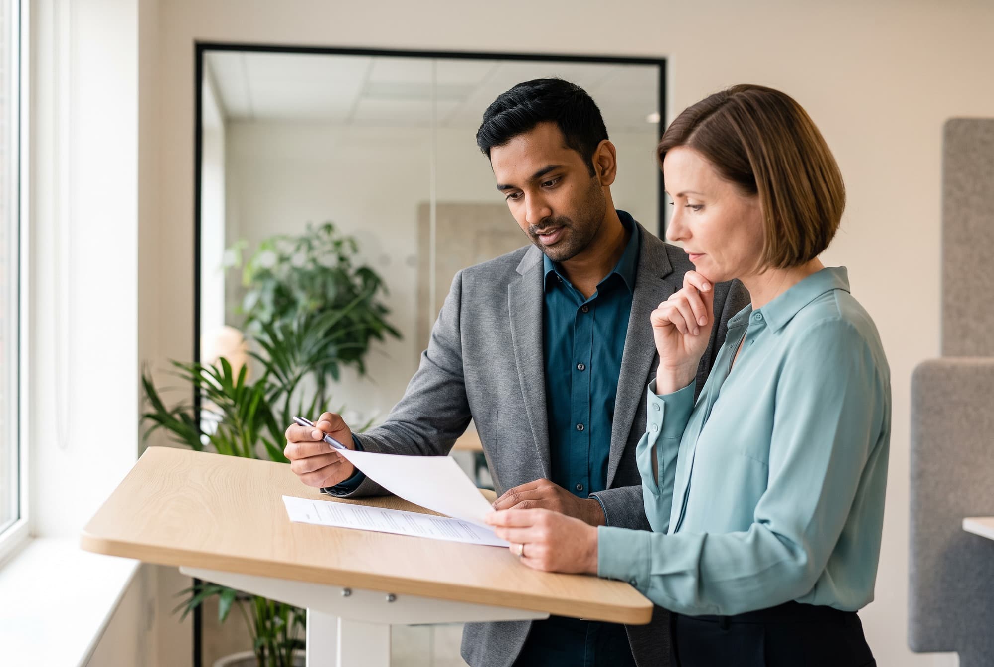 Two billing specialists reviewing a claim together at a standing desk